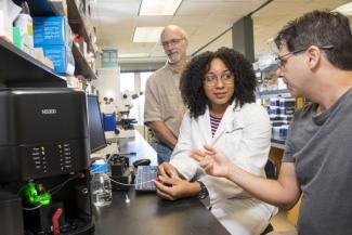 Jilarie Santos-Santiago, center, talks with faculty mentor Dr. Stephen Hajduk, background, and postdoctoral mentor Dr. Michael Cipriano